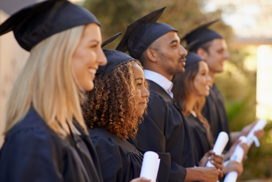 Row of confident and happy students wearing caps and gowns.