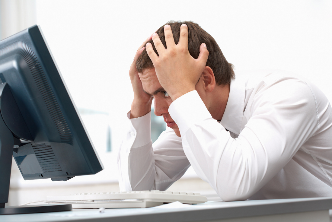 Stressed-out man with his hands on his head looking at a computer screen while worrying about the GRE's difficulty.