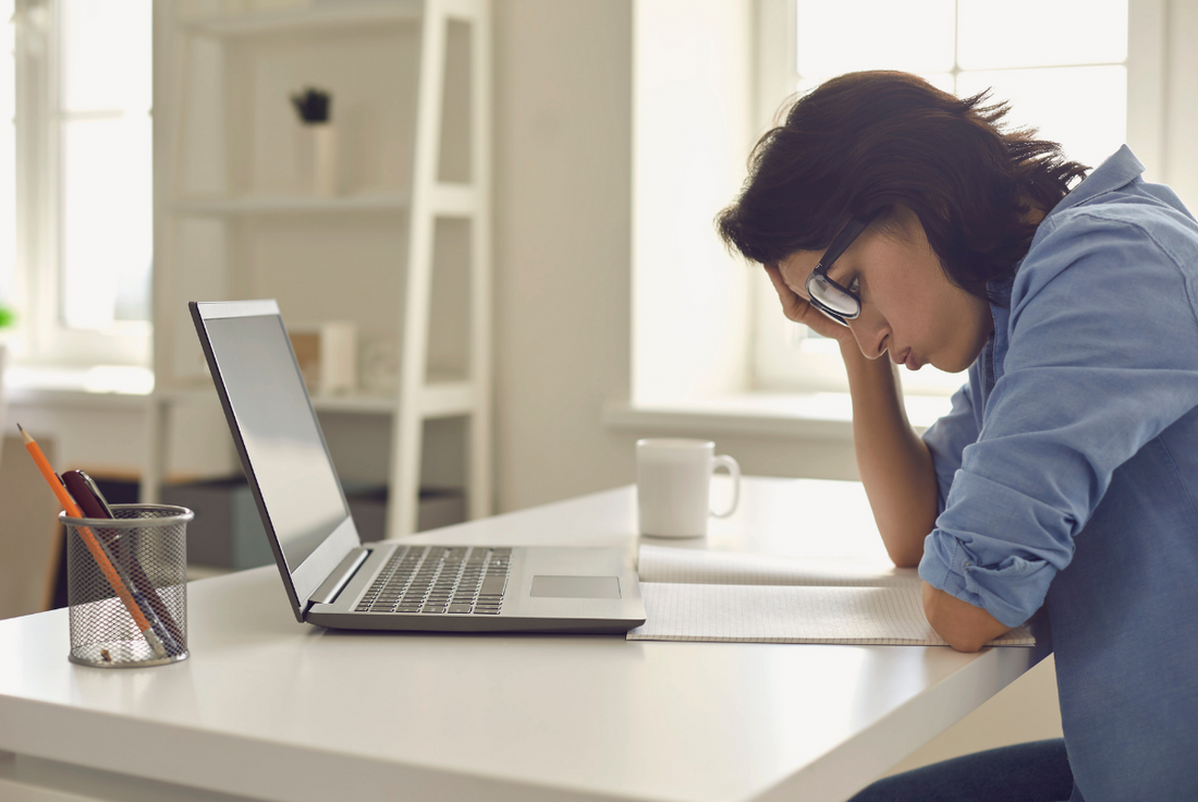 Woman sitting at a table with a laptop feeling overwhelmed by the GMAT exam.